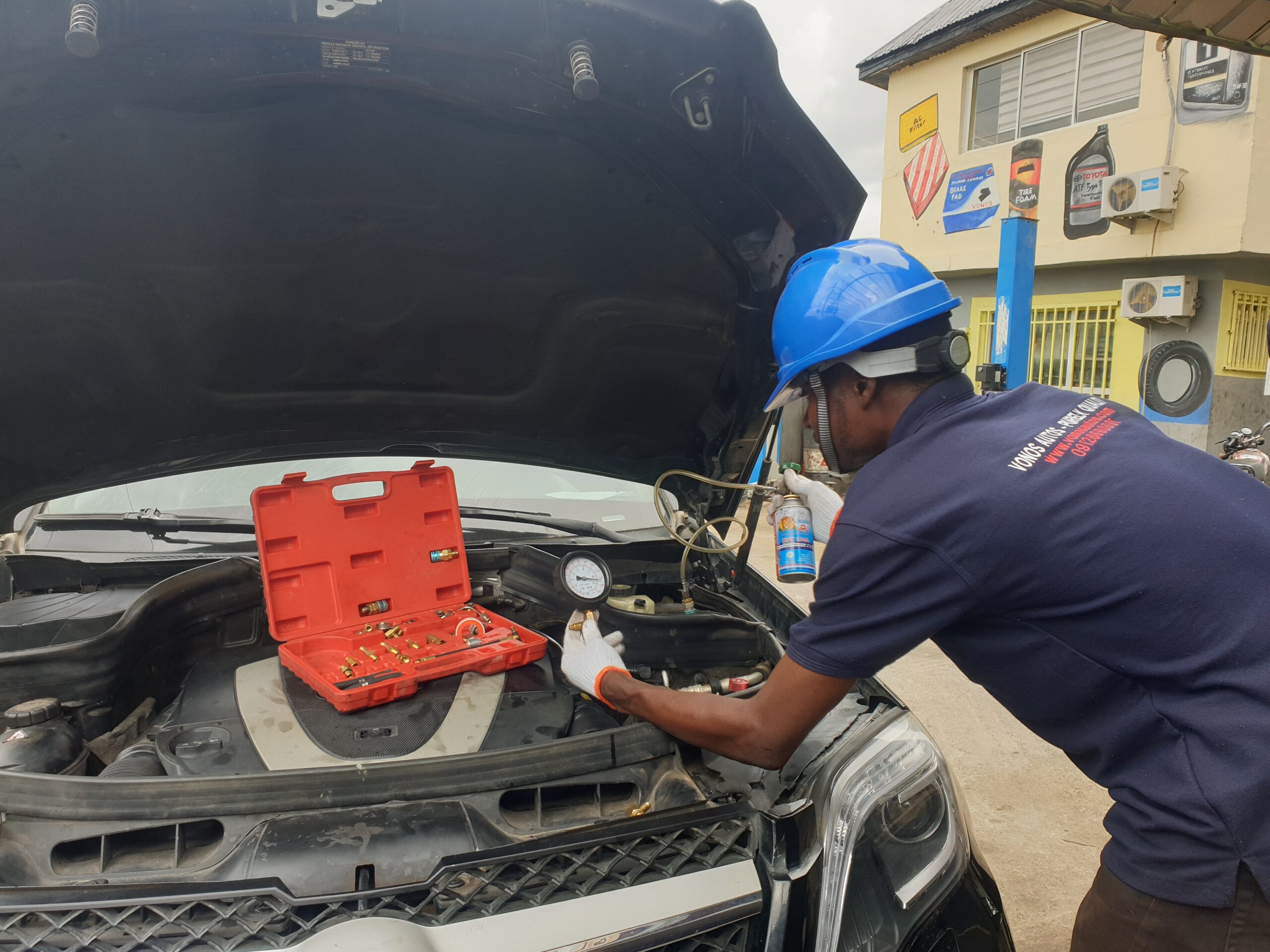 A technician performing an air conditioning refrigerant refill on a car. The technician is connecting a hose to the car's AC system to replenish refrigerant, addressing a common car AC problem and providing a solution for improved cooling performance.