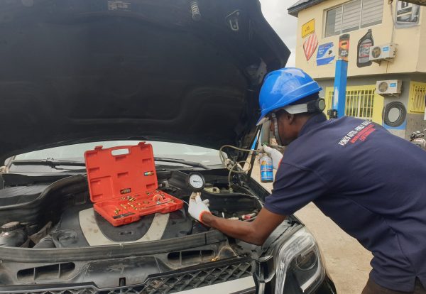 A technician performing an air conditioning refrigerant refill on a car. The technician is connecting a hose to the car's AC system to replenish refrigerant, addressing a common car AC problem and providing a solution for improved cooling performance.